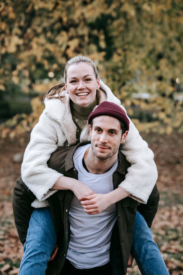 Um homem a dar boleia a uma mulher, com folhas secas no chão atrás deles.
