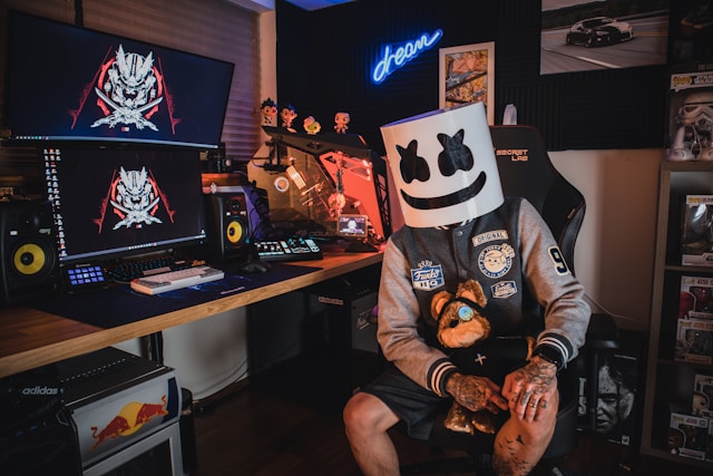 Um streamer do Twitch que usa uma máscara preta e branca enquanto está sentado numa cadeira de jogos em frente ao seu computador.