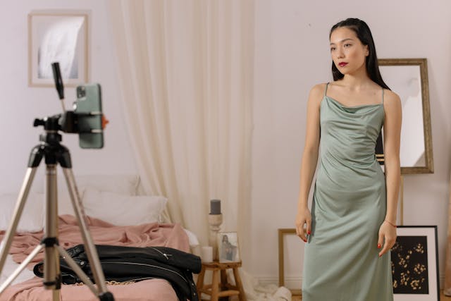 Uma mulher com um vestido verde posando em frente a um smartphone num tripé.