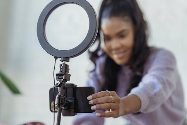 Grande plano de uma mulher sorridente a colocar o telemóvel num tripé com um anel de luz.