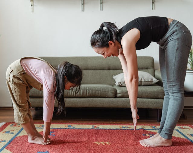 Uma mulher sorri enquanto faz exercício em casa com a sua filha.
