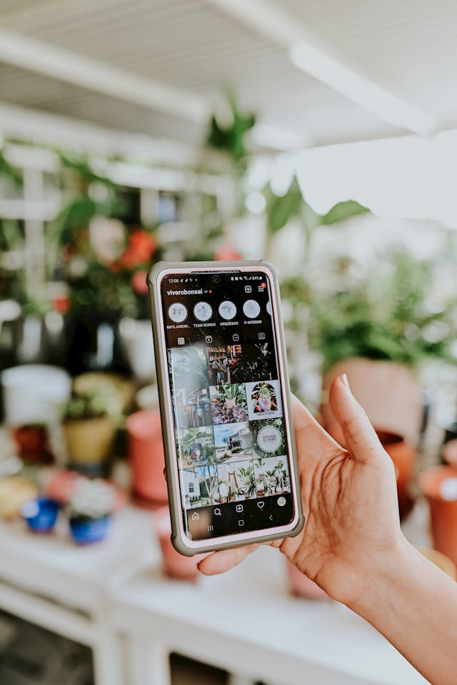 A person holding a smartphone with an Instagram profile displayed on the screen. 