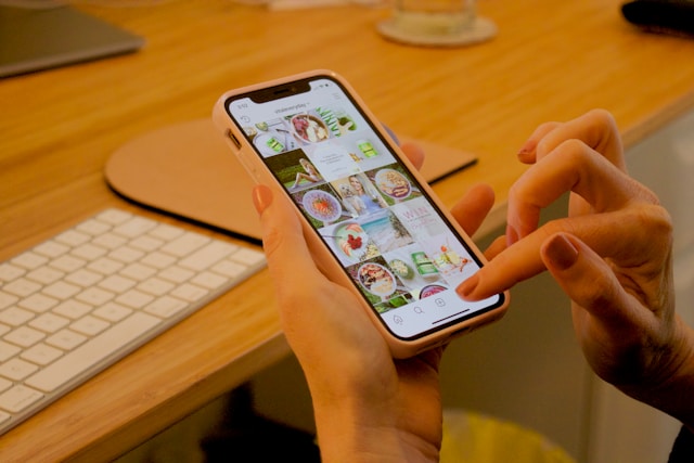 Cineva ține în mână un telefon cu aplicația Instagram deschisă. Telefonul arată un cont Instagram cu o serie de postări.