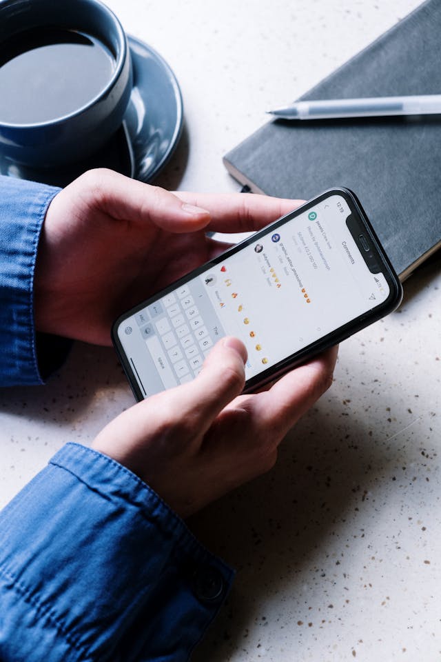Cineva ține în mână un telefon care arată secțiunea de comentarii de pe Instagram. Un comentariu este pe cale să fie adăugat care spune "Wow!" cu un emoji de foc.