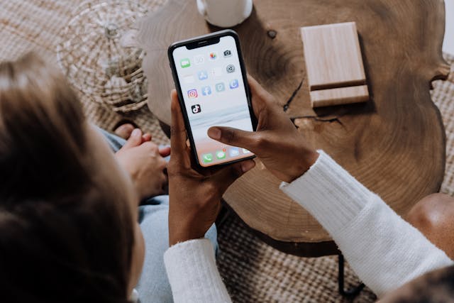 Două persoane se uită la un smartphone care afișează diferite aplicații, inclusiv TikTok.