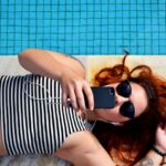 O persoană întinsă lângă o piscină și care navighează pe telefon.