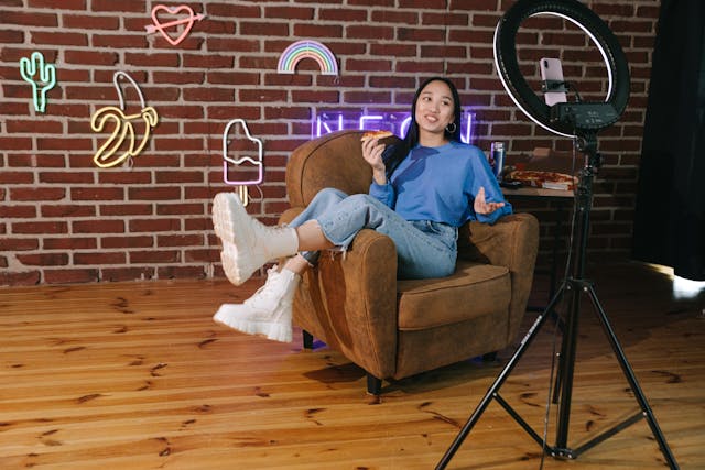 Un influencer se înregistrează în timp ce stă pe un scaun și mănâncă pizza.