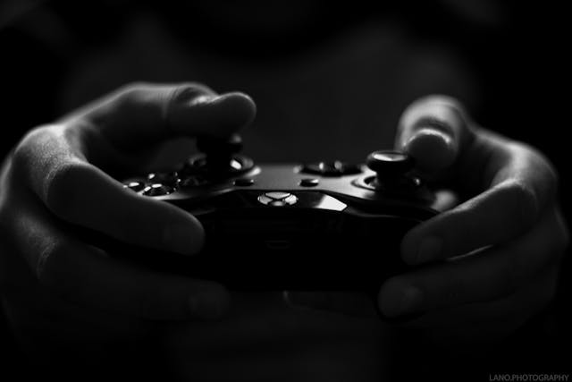O persoană ține în mână un controler de jocuri negru.