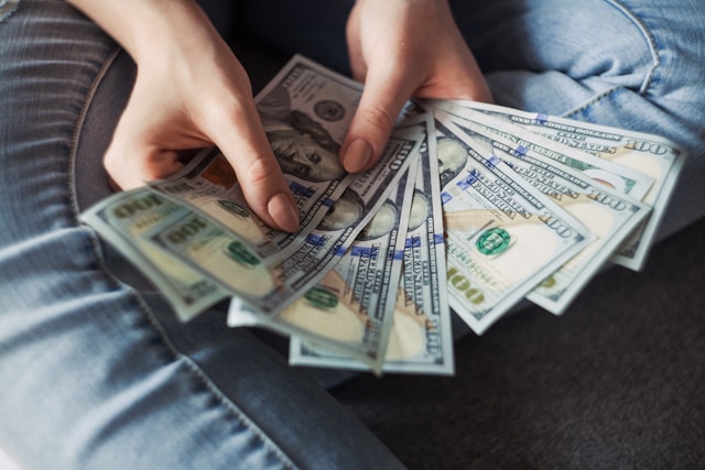 Cineva ține în mână o colecție de bancnote de 100 de dolari.