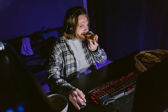 Un telespectator în flux stă la calculator și mănâncă pizza.